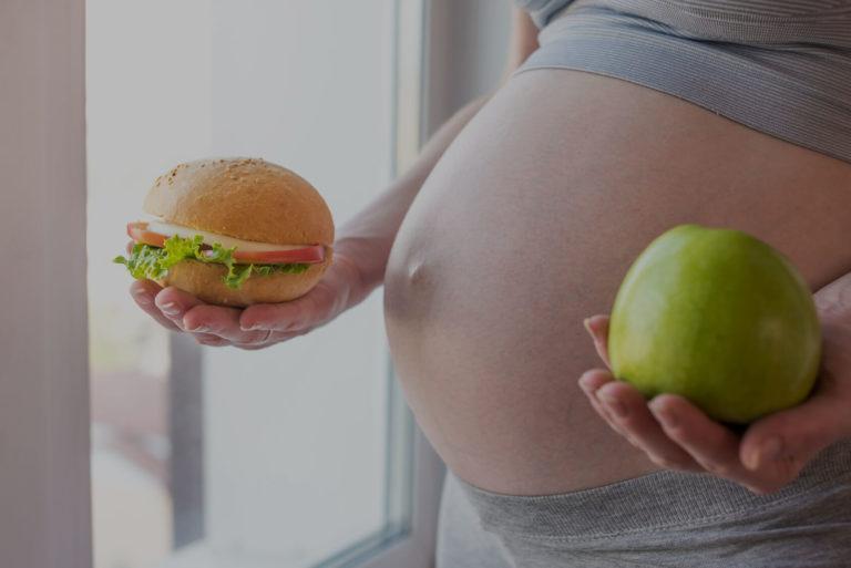 alimentation femme enceinte Ventre d'une femme enceinte avec une pomme dans la main gauche et un sandwich celle de droite