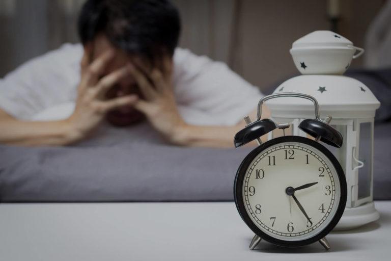 apnee du sommeil Homme brun allongé qui se tient la tête en regardant son réveil
