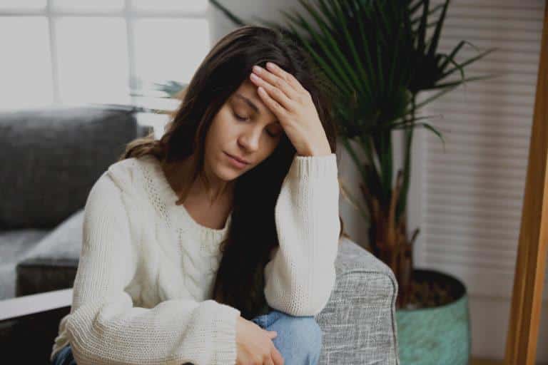anemie Jeune femme brune assise sur un canapé et se tenant la tête